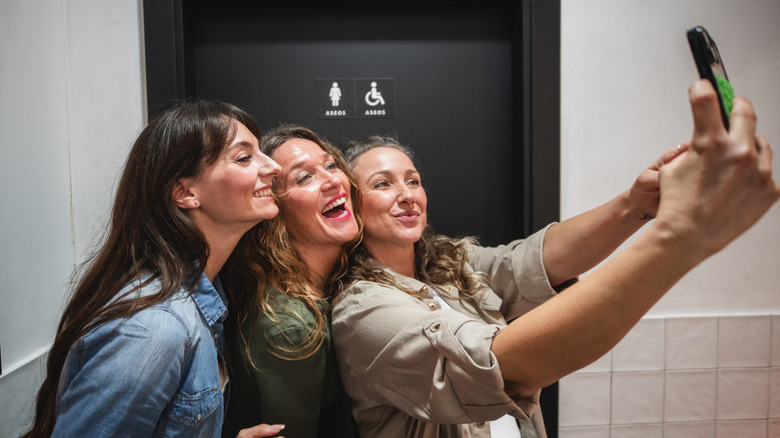women taking a selfie in a public bathroom
