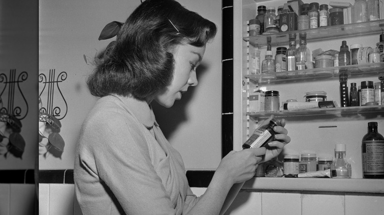 woman in 1950s looking at products in medicine cabinet