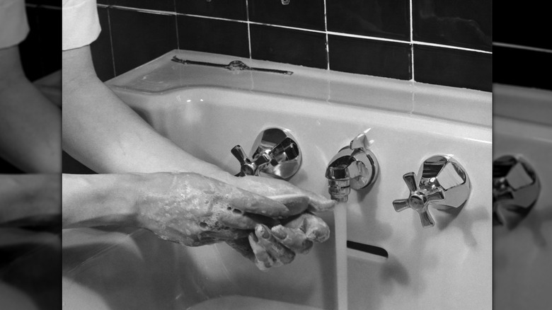 woman washing hands in 1950s sink with bar of soap