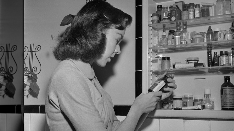 woman in 1950s looking at products in medicine cabinet