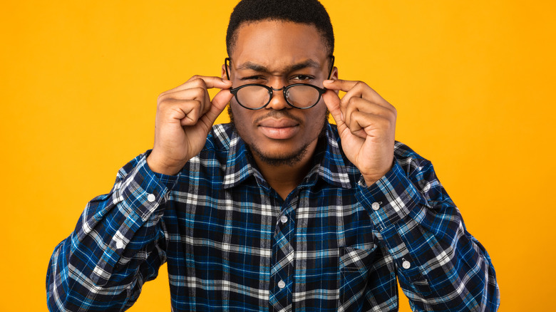 Man wearing eyeglasses and squinting his eyes, in front of yellow background