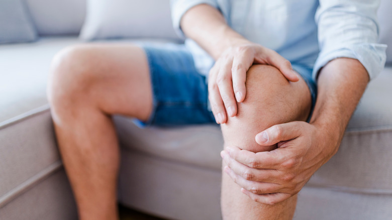 man on couch holding sore knee