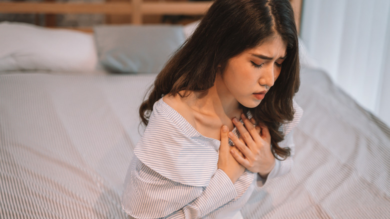 woman sitting on bed holding chest 