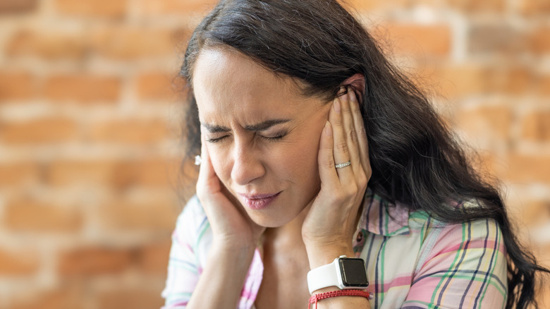 A woman holding her fingers to her ears while closing her eyes