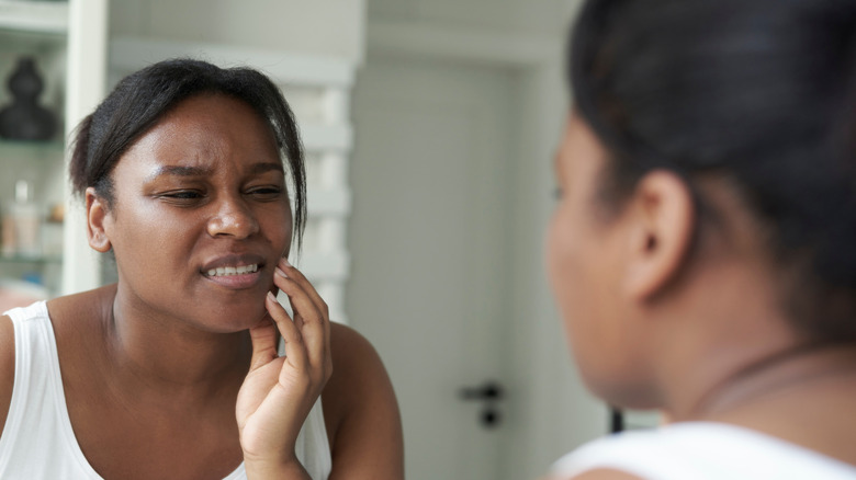 A woman wincing as she's looking in the mirror and holding her jaw