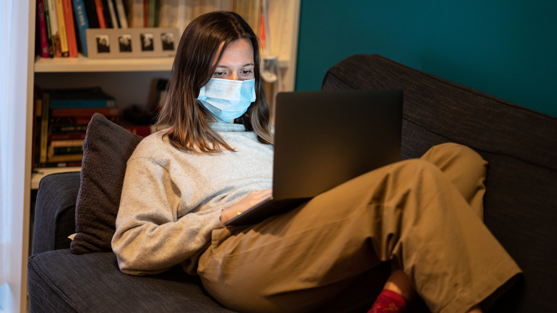 Woman wearing mask while working on laptop