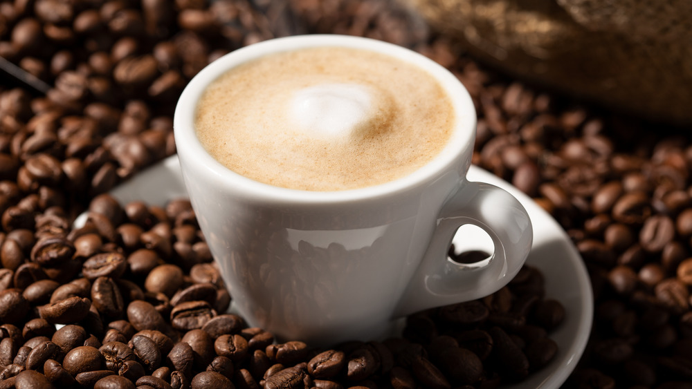 A milky coffee drink sitting on coffee beans 