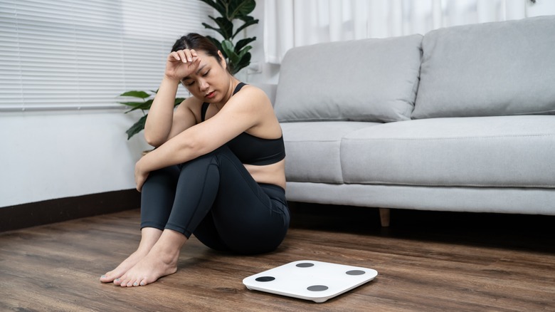 Frustrated woman sitting next to weight scale