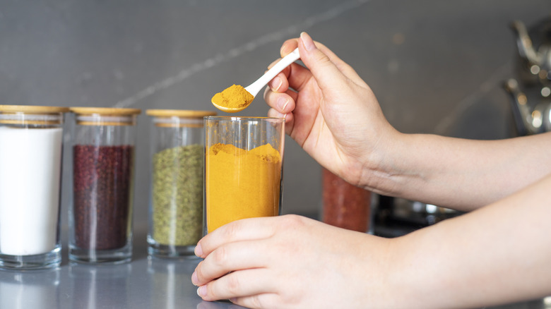 A woman's hand spooning out turmeric powder from a large jar