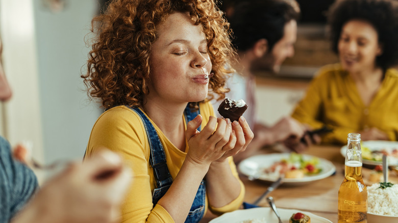 Woman with closed eyes tasting food among friends