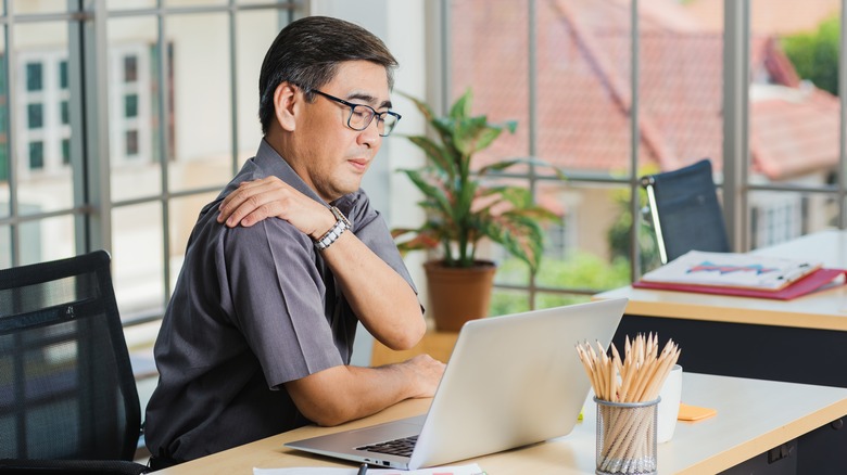 older man having shoulder pain while working at a desk