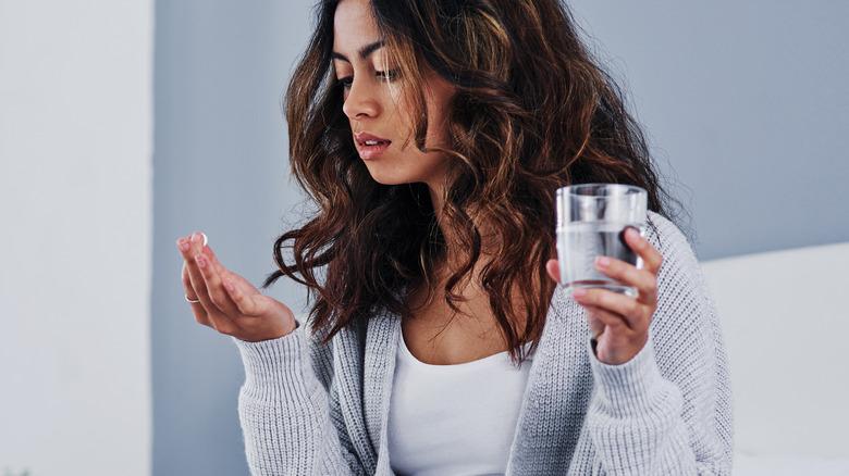 Woman holding ibuprofen pill and glass