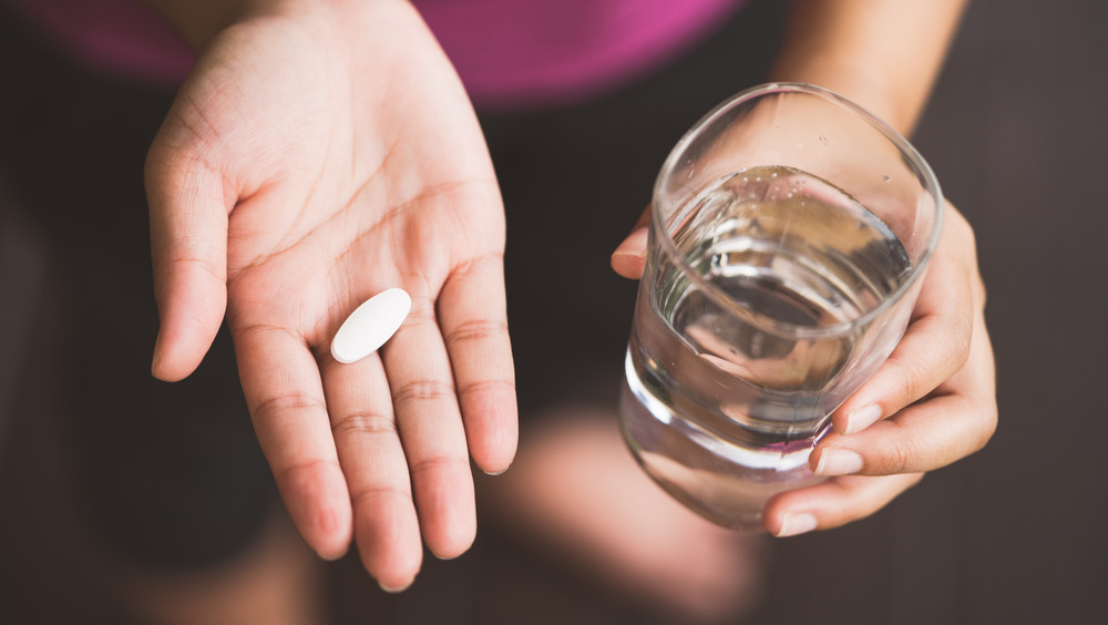 woman's hands holding a pill and a glass of water