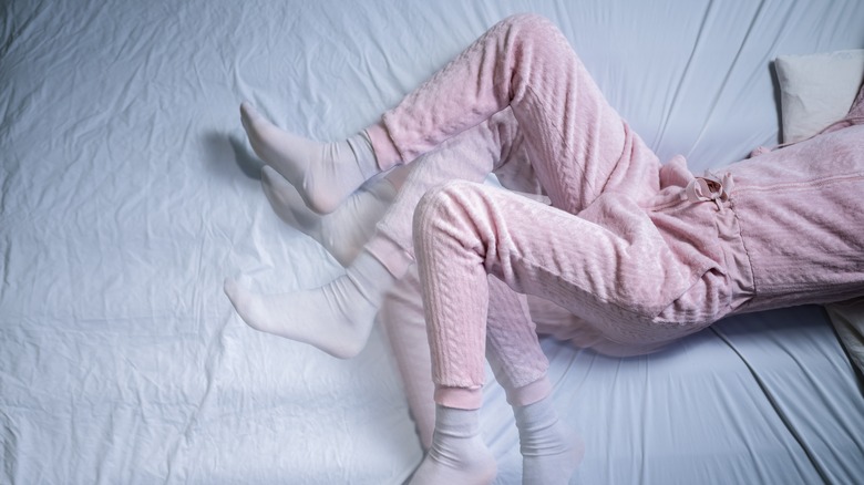 Woman in pink pjs with restless leg syndrome on bed