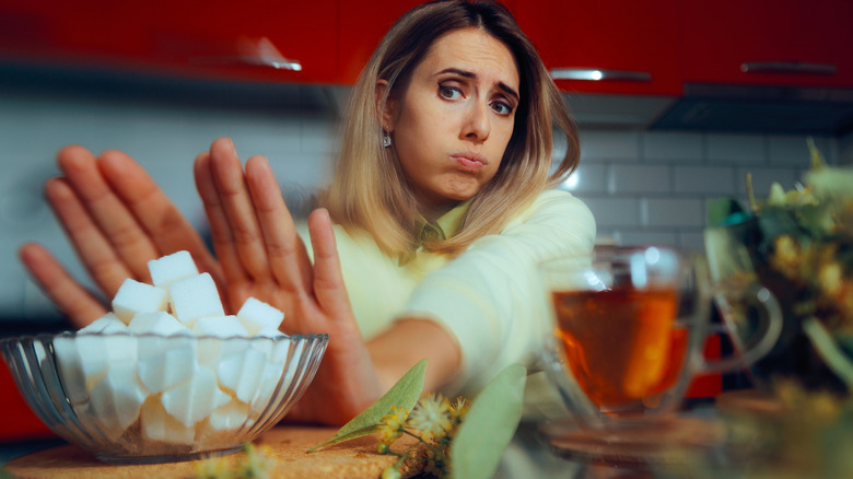 young woman pushing away sugar cubes at table