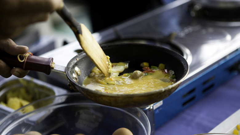 basket of whole eggs with a pan cooking an omelet