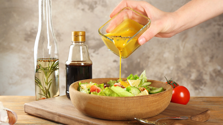 Someone pours honey mustard dressing onto their salad