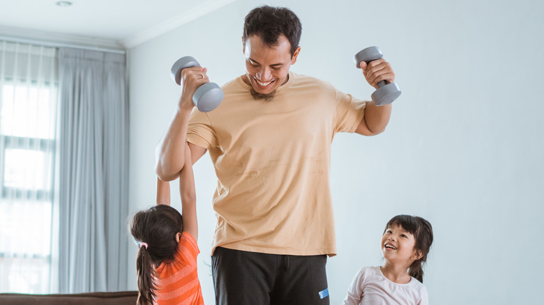 Man lifting hand weights smiling down at 2 kids