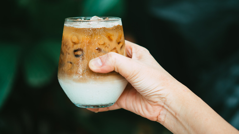 Someone holds a glass of sweetened iced coffee