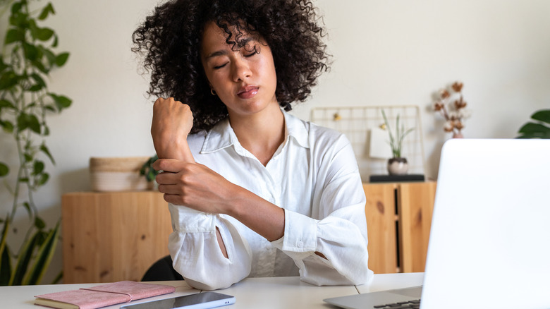 A woman sitting by a computer holding her painful wrist