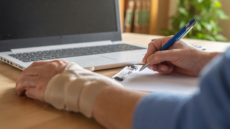 A person with a wrist splint filling out a paper form