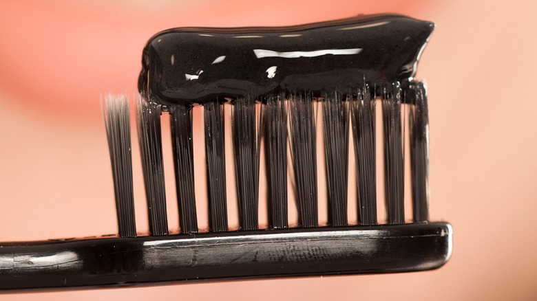 Glob of charcoal toothpaste on a toothbrush in front of a woman's smiling mouth