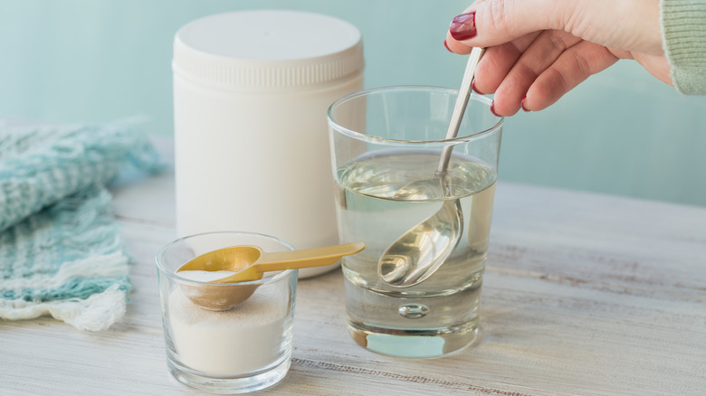 Someone stirs collagen powder into a glass