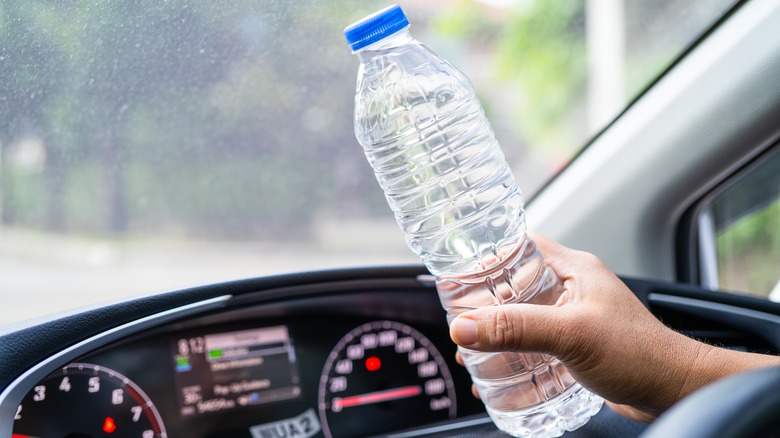 Hand holding an old plastic water bottle in the car