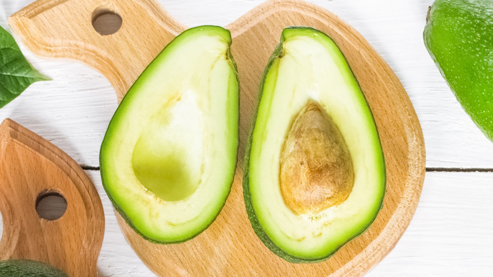 A fresh avocado cut in half on a wood cutting board