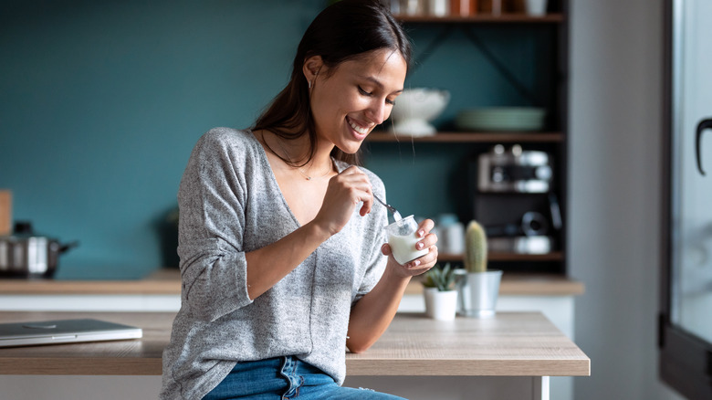 A woman eats yogurt in her kitchen.
