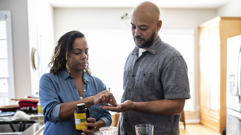 man and woman taking vitamins in kitchen