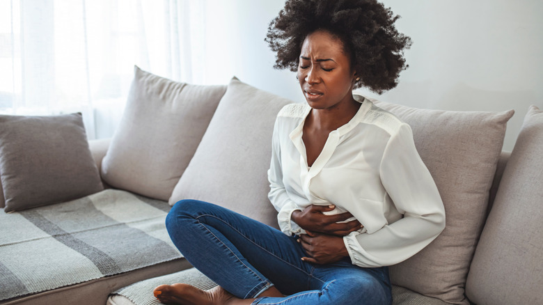 Woman sitting on sofa suffering from abdominal pain