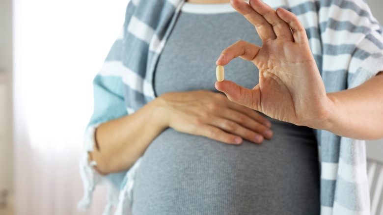 pregnant woman holding supplement capsule