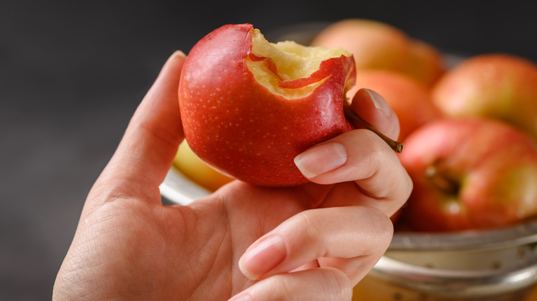 Close up of bitten red apple in hand and bowl full of red apples background