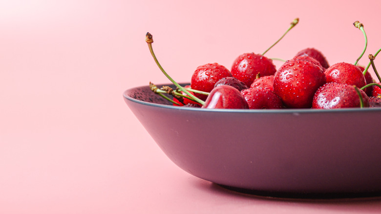 A bowl of cherries with a pink background
