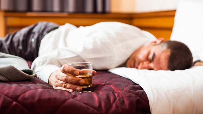 man asleep on the bed holding glass of whiskey