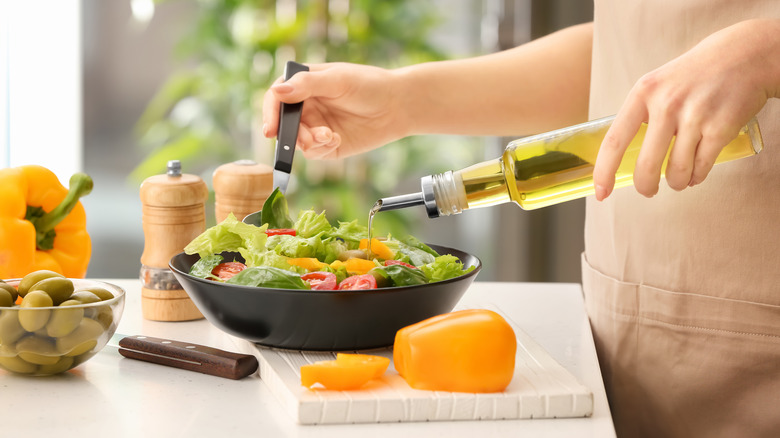 Someone pours olive oil in a bowl of salad