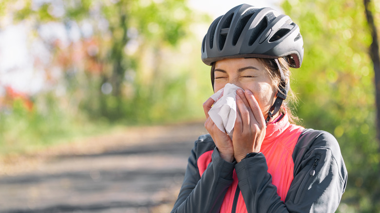 Woman with helmet on blowing her nose into a tissue while on outdoor bike ride