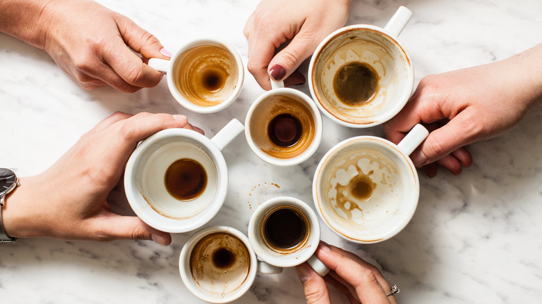 Top view of several people putting their used empty mugs together in a cluster