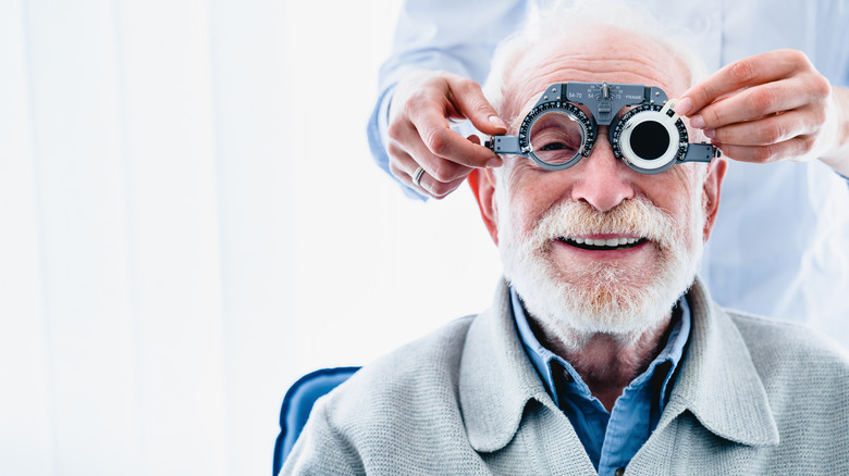 A man smiling as an eye doctor puts a vision testing apparatus over his face