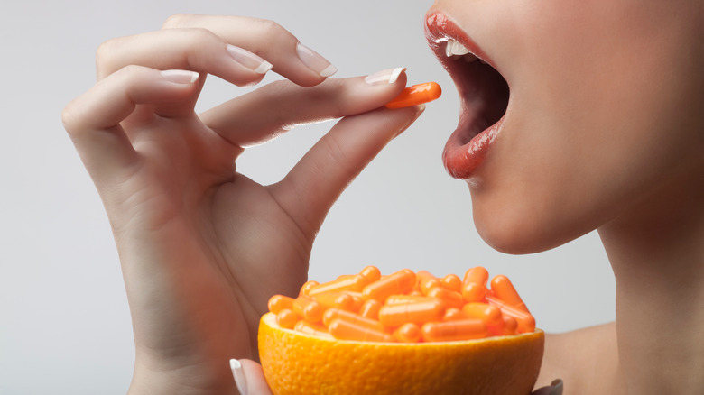 Woman putting orange capsule in mouth 