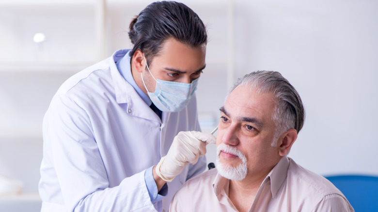 Man sitting getting ear checked by doctor wearing a mask and gloves