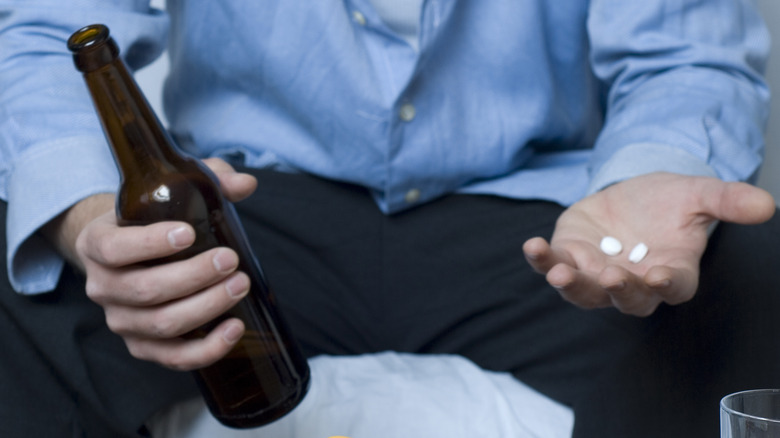 Man holding beer bottle and pills