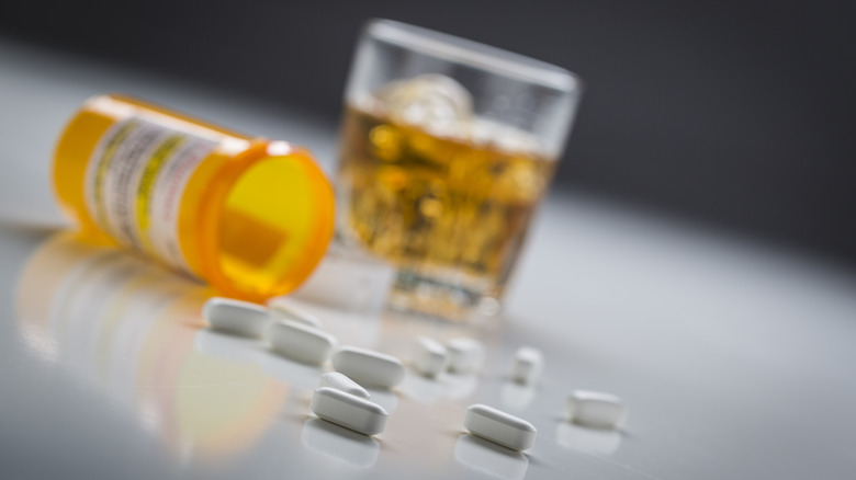 Several prescription drugs spilled from bottle near glass of alcohol