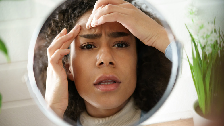 young woman examining her skin in a mirror with a worried expression 