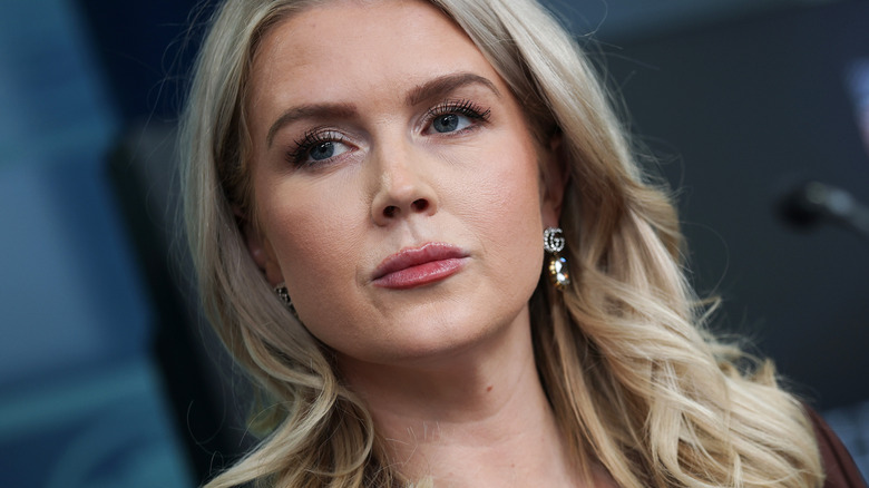 A titled angle photo of Karoline Leavitt behind a microphone.