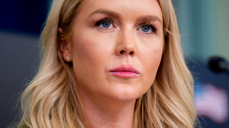 Close up of Karoline Leavitt with a stern expression, a blurred microphone points toward her.