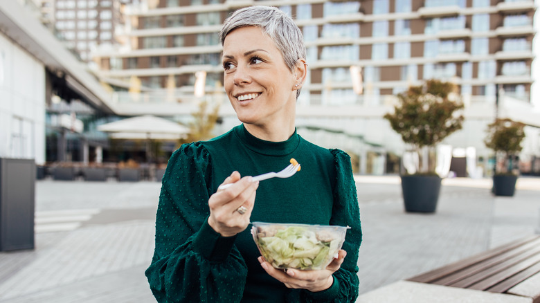 Woman eating from plastic container outdoors