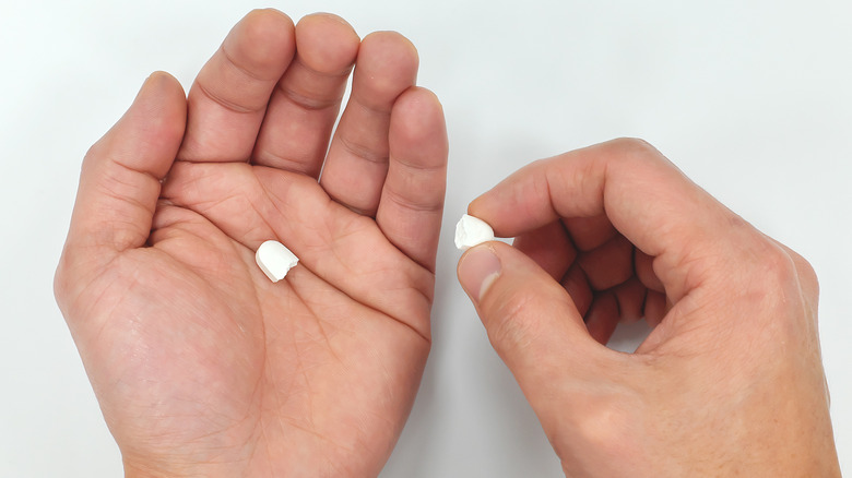 a persons hand holding a pill cut in half 
