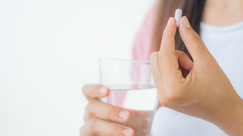 Closeup of woman holding pill in one hand and glass of water in the other
